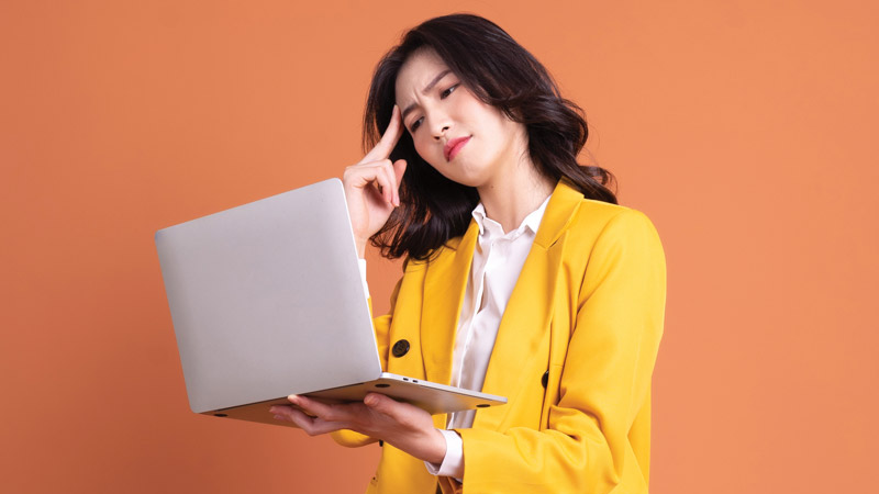 Mulher segura portátil na mão, a olhar para ecrã com ar confuso